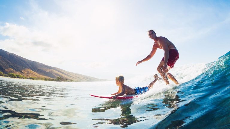 Young surfer learning to ride waves in Santa Teresa with parent nearby, enjoying a family-friendly surf session.