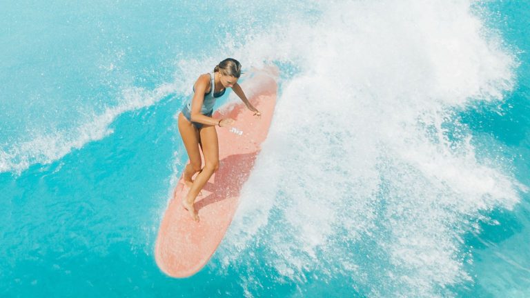 Beginner surfer riding a wave on a pink board in turquoise water, overcoming fear through surfing