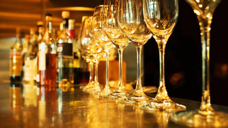 Elegant interior of a bar alicante with wine glasses lined up on a warmly lit counter and liquor bottles in the background.