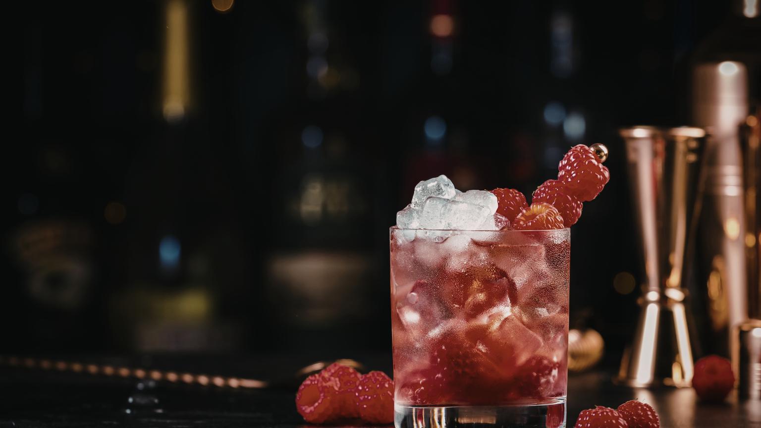 Cocktail con frambuesas y hielo servido en un bar Alicante con ambiente nocturno elegante