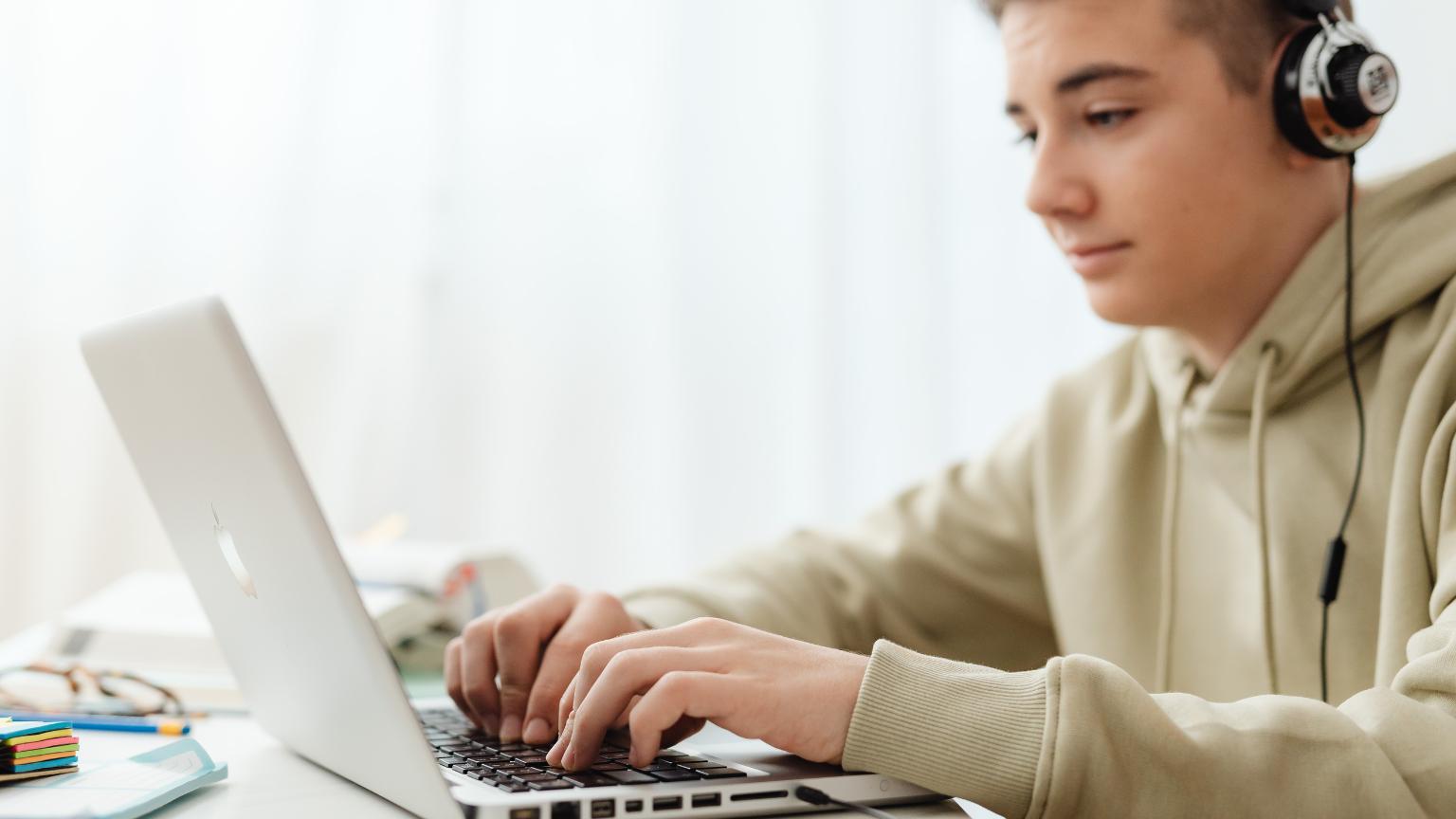 Student studying on a laptop at home while attending spanish classes online with headphones in a bright workspace.